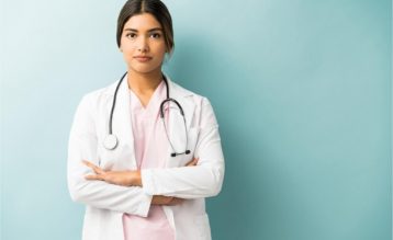 Attractive medical professional in uniform standing with arms crossed against isolated background